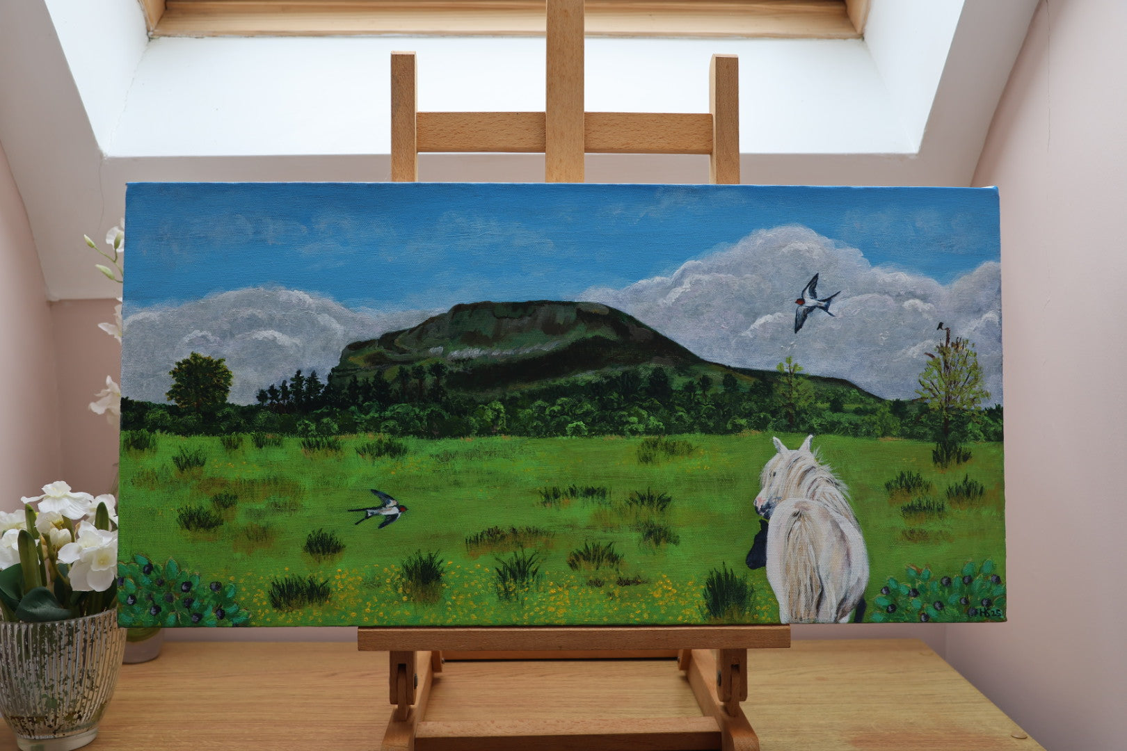 Painting of a landscape of Benlaughlin Mountain with a horse and two swallows on an easel indoors