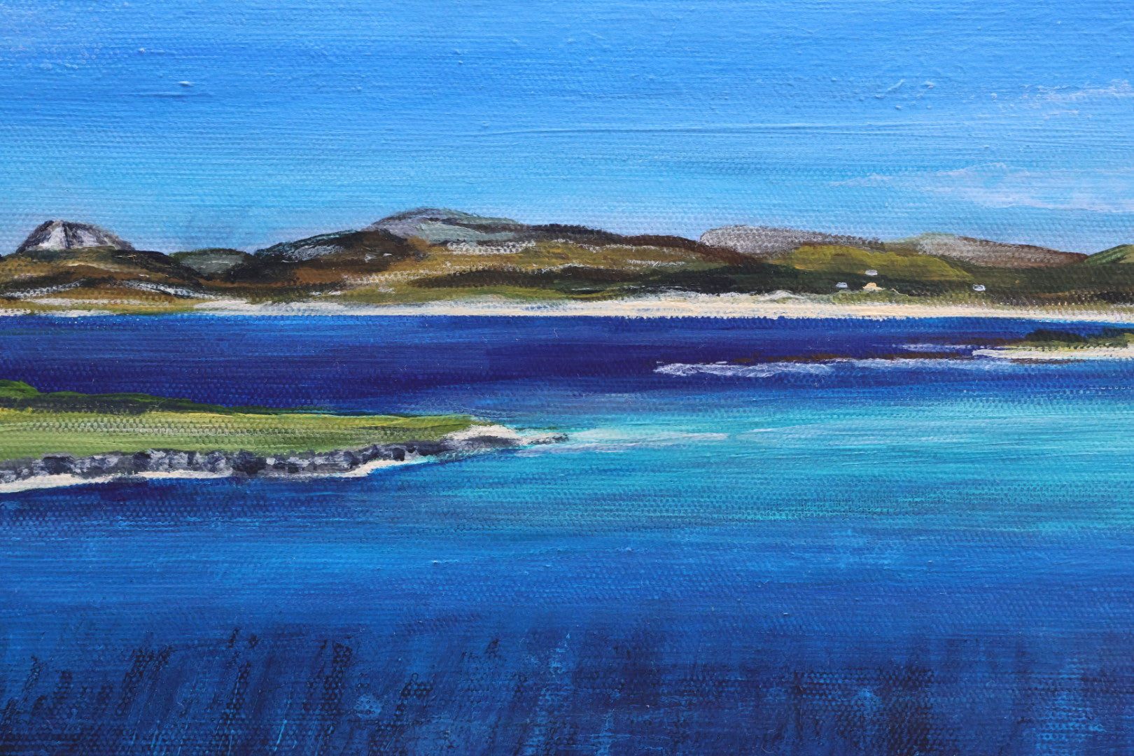 Coastal landscape with blue water and green hills under a clear sky