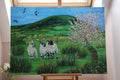 Painting of three lambs in a pastoral scene with hills and flowers on an easel.