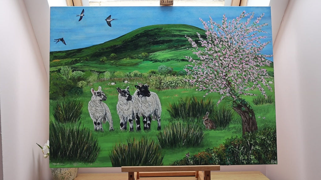Video of a painting featuring a green hill with three swallows in the sky. There’s a flowering apple tree, three lambs and an Irish hare in the green field. 